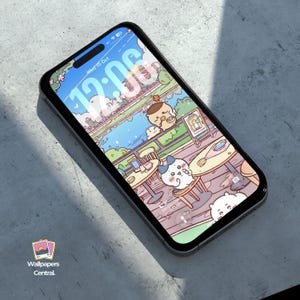 May include: A smartphone displays a whimsical cartoon scene of a cafe by a river, with cute animal characters. The screen shows the date and time. The phone is on a gray surface, with the "Wallpapers Central" logo in the corner.