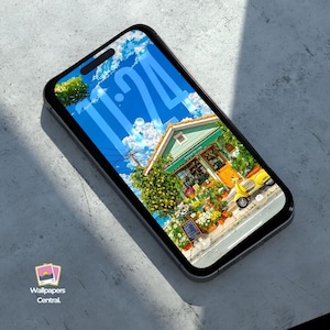 May include: A smartphone displays a vibrant wallpaper featuring a quaint shop with a green facade, yellow door, and a yellow scooter. The screen shows a blue sky with clouds and the time 11:24. The phone is black and rests on a gray surface.