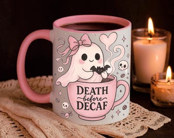 Puede incluir: Taza de café de cerámica con asa y borde rosas, con una linda ilustración de fantasma sosteniendo un murciélago y sentado en una taza de café. La taza dice "DEATH before DECAF" en escritura rosa. La taza está sobre un mantel individual de encaje, con velas encendidas al fondo.