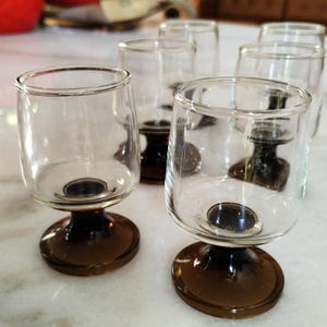 Può includere: Set di sei bicchieri da liquore in vetro trasparente con steli e basi marroni. I bicchieri hanno una forma a calice arrotondata e un gambo corto. Le basi circolari garantiscono stabilità. Adatti per servire liquori.