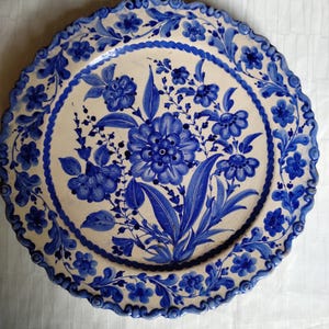 Puede incluir: Un plato de cerámica con base crema y detallados diseños florales azules. El plato tiene un borde festoneado y un ramo floral central, con más diseños florales en el borde. Diámetro aproximado de 30 cm.