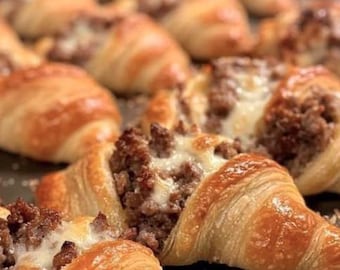 May include: Close-up of several baked croissants filled with a savory mixture of ground meat and melted cheese. The croissants have a golden-brown, flaky crust, and the filling is visible in the center.