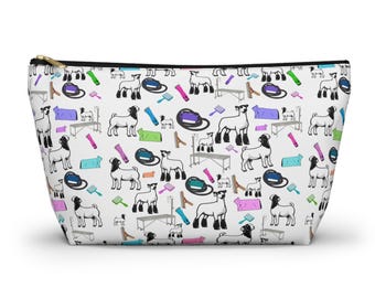 Puede incluir: Bolsa blanca con cremallera con un patrón repetido de cabras en blanco y negro, herramientas de aseo y mesas de exhibición. El patrón incluye elementos azules, morados, rosas, verdes y beige. La bolsa tiene una cremallera dorada.