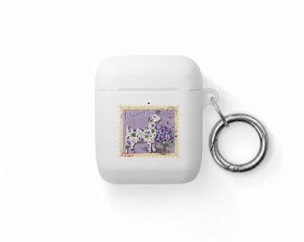 Puede incluir: Una funda protectora blanca para auriculares inalámbricos con un gráfico rectangular de una cabra con estampado de flores moradas junto a un ramo de violetas, el texto February y un mosquetón circular de metal plateado en el lateral.