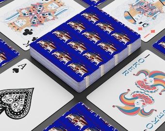 Puede incluir: Una baraja de cartas con una cubierta azul con un diseño de bandera estadounidense y un águila. Las cartas individuales rodean la baraja, incluyendo un Rey de Tréboles, un As de Picas y una carta de Joker.