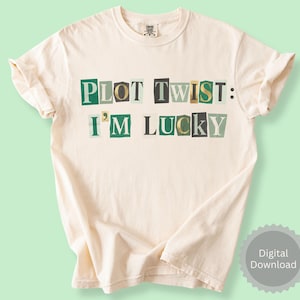 May include: Cream-colored t-shirt with the text "PLOT TWIST: I'M LUCKY" in a collage-style font using green, black, and gold letters. The shirt has rolled-up sleeves and a round neckline. A digital download badge is in the bottom right corner.