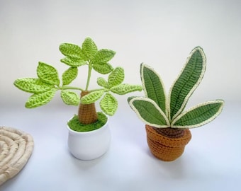 May include: Two crochet plants are displayed on a white surface. One plant has bright green leaves and a brown stem, potted in a white ceramic pot. The other plant has green leaves with white edges, in a brown pot. The plants are handmade.