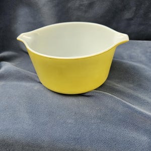 May include: A yellow mixing bowl with a white interior. The bowl has a rounded shape with two small handles on either side. The exterior is a solid, bright yellow, while the interior is white.