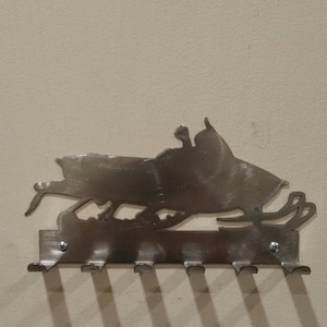 May include: A metal snowmobile silhouette wall hook with six hooks. The hook is made of brushed stainless steel and has a rustic look.