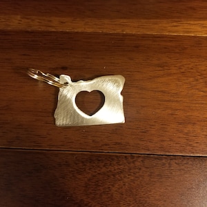 May include: A silver metal keychain shaped like the state of Oregon with a heart cut out in the centre.