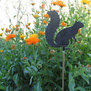 May include: A black metal silhouette of a squirrel is mounted on a stick and placed in a garden with orange and yellow flowers.
