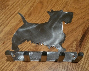 May include: A silver metal key holder shaped like a Scottish Terrier dog with five hooks. The dog is standing on a metal base with the hooks attached to the base.