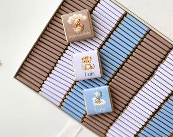 May include: A box of chocolate bars with baby-themed designs. The chocolates have images of a teddy bear, a tiger, and a hot air balloon. Some chocolates have the name "Luis" printed on them, and one says "Welcome Baby". The box has a white, blue, and brown color scheme.