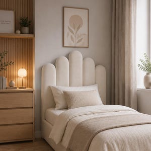 May include: A cream-colored upholstered bed frame featuring a tall, scalloped headboard with vertical panels. The bed is dressed in neutral-toned bedding, including a textured throw blanket and a rectangular accent pillow, creating a cohesive look.