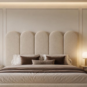 Op de afbeelding: Een kingsize bed met een hoog, beige, gestoffeerd hoofdeinde met vijf verticale boogpanelen. Het bed is opgemaakt met lichtbeige beddengoed, donkerbruine sierkussens en een donkerbruine sprei, geflankeerd door twee nachtkastjes met een marmeren blad.