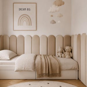 Può includere: Una struttura letto bianca con testiera imbottita beige composta da pannelli verticali arrotondati. Il letto include un cuscino beige a motivi e una coperta beige tinta unita. Sopra è appesa una stampa incorniciata con un arcobaleno e il testo DREAM BIG.