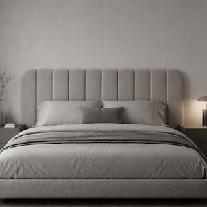Può includere: Una struttura letto imbottita color grigio chiaro con una testiera alta a canali verticali. Il letto è vestito con biancheria coordinata color grigio chiaro, inclusi due cuscini e un plaid. Due comodini grigio scuro fiancheggiano il letto.