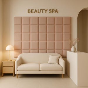 Può includere: Un divano beige a due posti è posizionato davanti a un grande pannello a parete color rosa polvere con motivo a quadrati. Sopra il pannello, la scritta BEAUTY SPA è in lettere dorate. Sono presenti un comodino in legno chiaro e un bancone bianco.