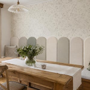 Puede incluir: Comedor rústico con mesa de madera, camino de mesa blanco y jarrón con flores. La habitación cuenta con un banco empotrado con cojín verde y papel pintado floral. Una lámpara decorativa cuelga del techo.