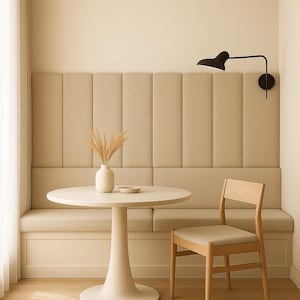 Puede incluir: Un comedor moderno con una mesa redonda, un banco y una silla de madera. La mesa tiene un jarrón con flores secas y un plato pequeño. Las paredes son de color neutro y una lámpara negra está montada en la pared.