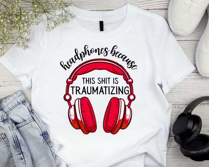 May include: White t-shirt with a red and white graphic of headphones. The text on the shirt reads "headphones because THIS SHIT IS TRAUMATIZING". The shirt is paired with blue jeans and white sneakers.