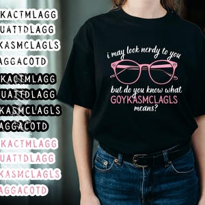 May include: Black t-shirt with the text "i may look nerdy to you but do you know what GOYKASMCLAGLS means?" in pink. The design includes pink glasses. The shirt is paired with blue jeans.