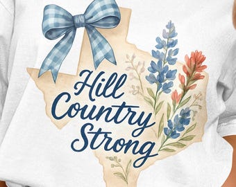 May include: White t-shirt featuring a watercolor design. The design includes a blue gingham bow, the outline of Texas, and the words "Hill Country Strong" in a script font. Floral accents in blue and red complete the design.