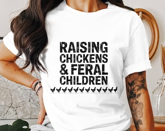 Puede incluir: Camiseta blanca con el texto "RAISING CHICKENS & FERAL CHILDREN" en letras negras. Debajo del texto hay una fila de pequeñas siluetas de pollos negros. La camiseta es una prenda informal para el día a día.