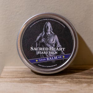 Peut inclure: Une boîte métallique ronde de baume à barbe Sacred Heart. L'étiquette présente un fond noir avec une image blanche de Jésus et le texte "Sacred Heart Beard Balm" et "Catholic Balm Co."