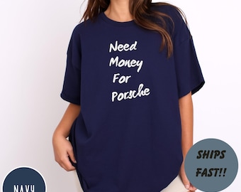 May include: Navy blue t-shirt with the text "Need Money For Porsche" in white script. The shirt has a relaxed fit and short sleeves. A navy circle with the word "NAVY" is in the lower left corner. A gray circle with the words "SHIPS FAST!!" is in the lower right corner.