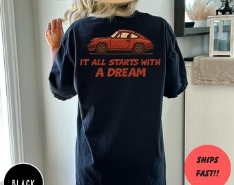 May include: Black t-shirt with a red car graphic and the text "IT ALL STARTS WITH A DREAM". The car is a classic style. The shirt has short sleeves and a relaxed fit.