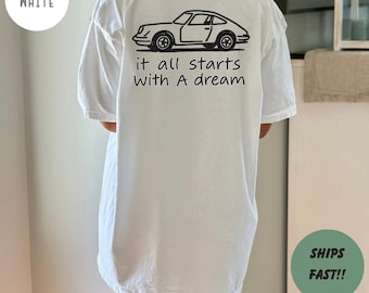 May include: White t-shirt with a black car graphic and the text "it all starts with A dream". The shirt is a casual style, suitable for everyday wear. The shirt is white.