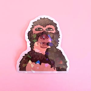 Puede incluir: Una pegatina holográfica con un mono de dibujos animados con una expresión pensativa. El mono tiene pelaje marrón, una cara rosada y se toca los labios con un dedo. La pegatina tiene un borde blanco y está sobre un fondo rosa.