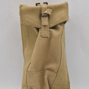 Könnte beinhalten: Beige Canvas-Beutel mit Klappenverschluss und schwarzer Schnalle. Der Beutel hat eine rechteckige Tasche auf der Vorderseite und besteht aus einem strapazierfähigen, strukturierten Stoff. Die Tasche ist zum Tragen konzipiert.