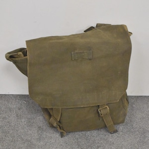May include: An olive green canvas messenger bag with a flap closure and adjustable straps. The bag has a rectangular shape with a buckle closure and a small strap detail on the front. The bag is made of a durable, rugged material.