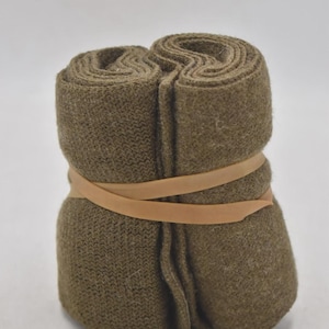 May include: A bundle of olive green socks, rolled and secured with a tan rubber band. The socks appear to be made of a thick, knitted material, suggesting warmth and comfort. The neutral color palette and simple presentation highlight the utilitarian nature of the product.