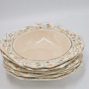 May include: A stack of five cream-colored ceramic bowls with scalloped edges. The wide rims feature a crackled mosaic pattern decorated with small, hand-painted orange and blue flowers and green leaves, finished with a thin gold-tone trim.