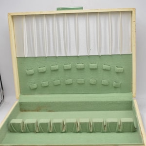 Może przedstawiać: Otwarta, zabytkowa skrzynka do przechowywania sztućców z jasnozielonym filcowym wnętrzem i kremowym wykończeniem. Pudełko posiada wiele przegródek do przechowywania sztućców i białą podszewkę.