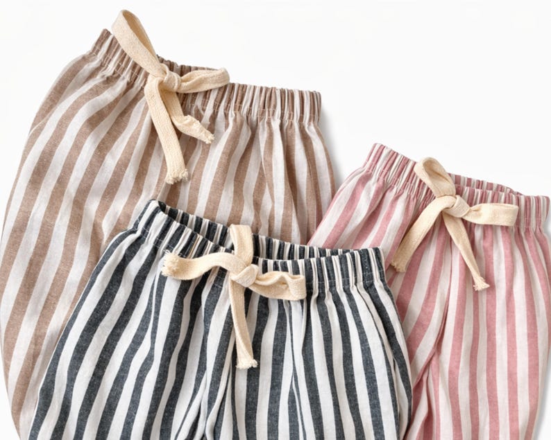 Puede incluir: Primer plano de tres pares de pantalones cortos a rayas en varios colores: marr&oacute;n y blanco, azul marino y blanco y rosa y blanco. Cada par tiene una cintura con cord&oacute;n y un lazo color crema. Los pantalones cortos son de tela ligera.