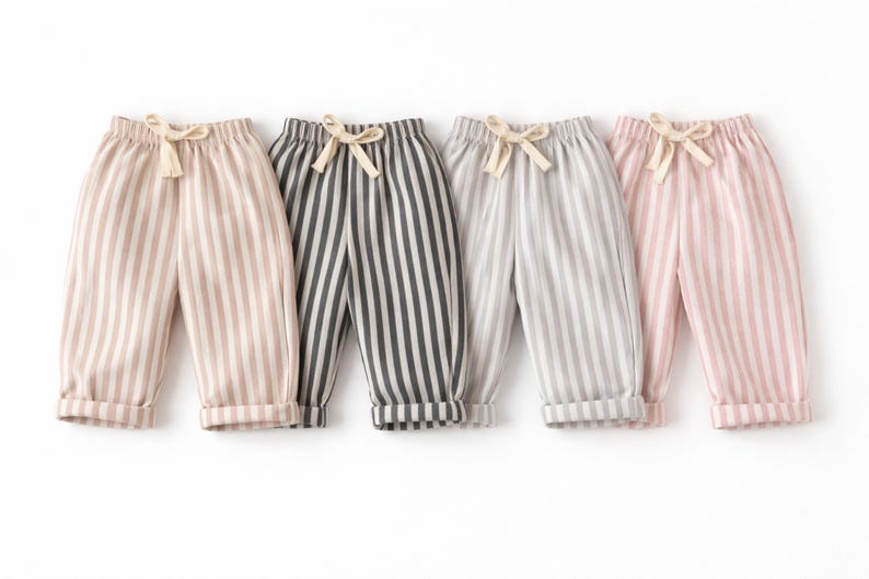 Puede incluir: Cuatro pantalones a rayas en beige, gris oscuro, gris claro y rosa. Cada par tiene rayas verticales, cintura con cord&oacute;n y dobladillos. Los pantalones est&aacute;n dise&ntilde;ados para ni&ntilde;os.