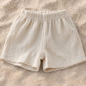 May include: Cream-colored shorts with an elastic waistband. The shorts are made of a textured fabric and appear lightweight. The garment is suitable for warm weather and casual wear.