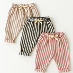 Puede incluir: Tres pantalones a rayas en colores neutros: beige, negro y blanco, y rosa y blanco. Cada par tiene un lazo de cord&oacute;n en la cintura y dobladillos con vuelta. Los pantalones son probablemente para ni&ntilde;os.