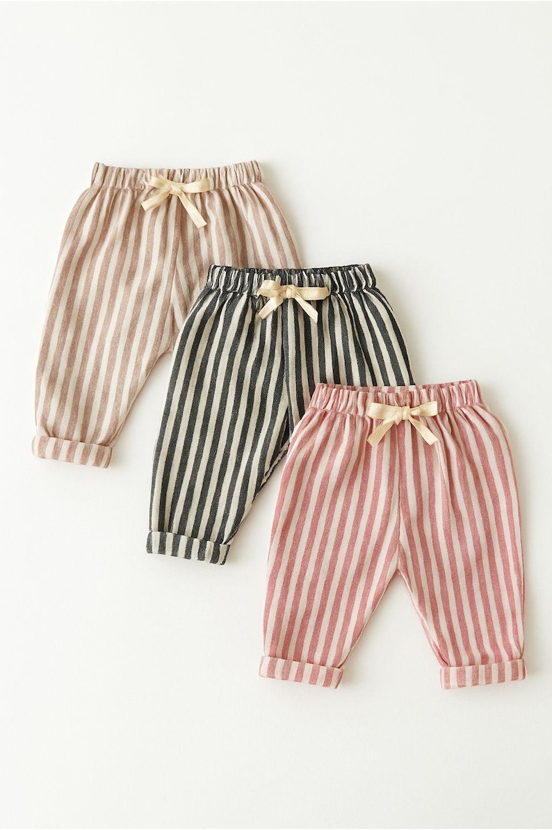 Puede incluir: Tres pantalones a rayas en colores neutros: beige, negro y blanco, y rosa y blanco. Cada par tiene un lazo de cord&oacute;n en la cintura y dobladillos con vuelta. Los pantalones son probablemente para ni&ntilde;os.
