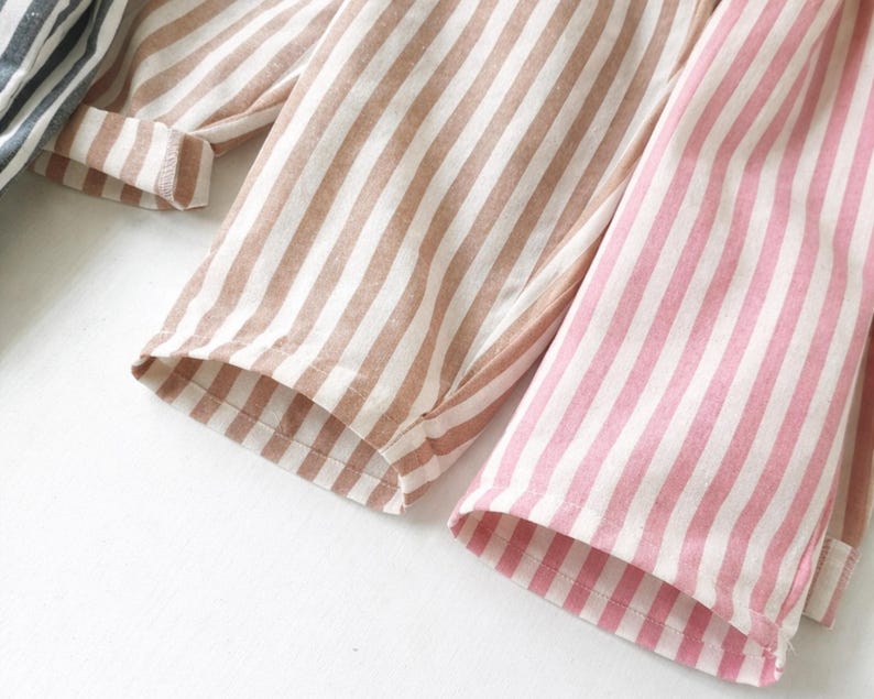 Puede incluir: Primer plano de tres pares de pantalones de pijama a rayas en diferentes colores. Un par es rosa y blanco, otro es marr&oacute;n y blanco, y el tercero es azul y blanco. La tela es suave y los pantalones tienen un corte holgado.