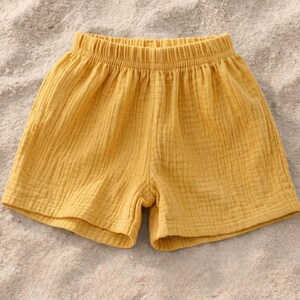 May include: Mustard yellow shorts with an elastic waistband. The shorts are made of a textured fabric and appear lightweight. The garment is designed for casual wear.