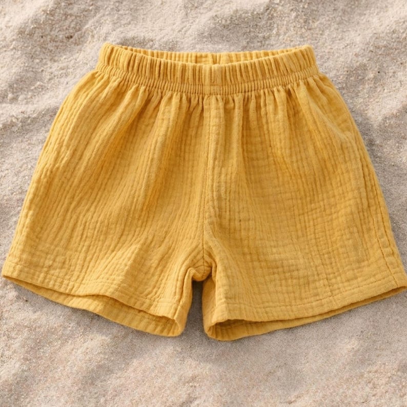 May include: Mustard yellow shorts with an elastic waistband. The shorts are made of a textured fabric and appear lightweight. The garment is designed for casual wear.
