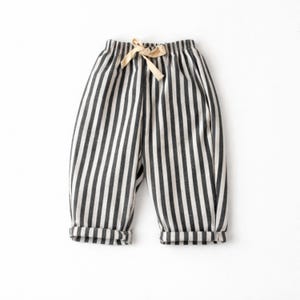 Puede incluir: Pantalones a rayas blancas y negras con cintura con cord&oacute;n y pu&ntilde;os doblados. Los pantalones est&aacute;n hechos de una tela suave y son adecuados para ropa casual. Las rayas verticales crean un dise&ntilde;o visualmente atractivo.
