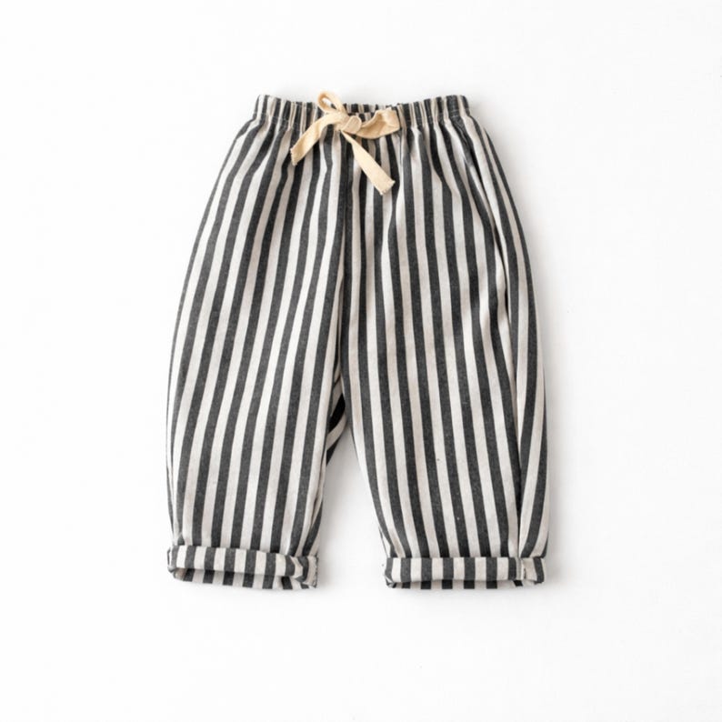 Puede incluir: Pantalones a rayas blancas y negras con cintura con cord&oacute;n y pu&ntilde;os doblados. Los pantalones est&aacute;n hechos de una tela suave y son adecuados para ropa casual. Las rayas verticales crean un dise&ntilde;o visualmente atractivo.