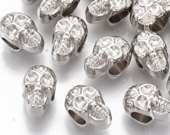 May include: A group of silver skull-shaped beads. The beads are detailed with raised eye sockets and teeth.