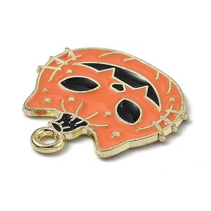 以下が含まれることがあります： 黒目の口のあるジャック・オ・ランタンの形をした金色の金属製チャーム。チャームの上部にネックレスやブレスレットに取り付けるためのループがあります。